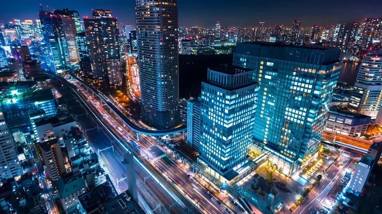 Night aerial view of illuminated downtown cityscape with tall office buildings and light trails from traffic on busy streets